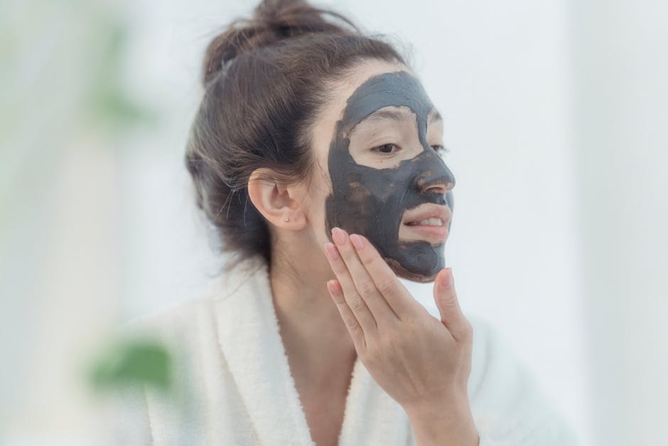 A woman in a bathrobe applies a charcoal beauty mask, promoting skincare and relaxation