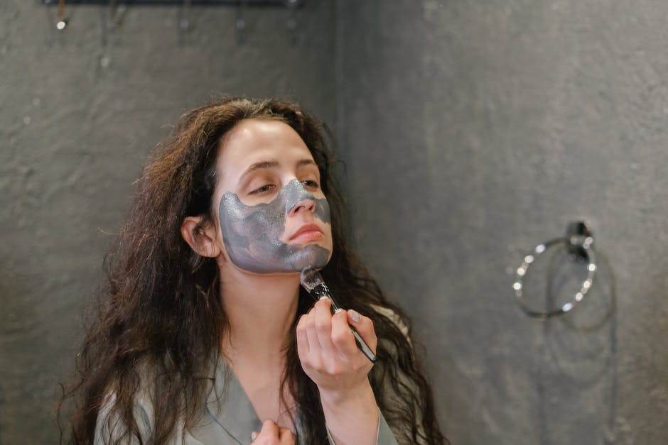 A woman applies a facial mask as part of her skincare routine in a modern bathroom
