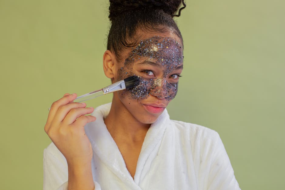 African American woman in bathrobe applies a glitter face mask in a studio portrait